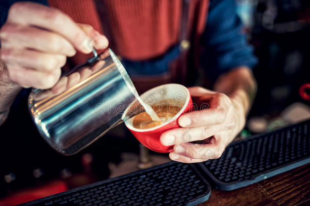 咖啡师用牛奶在长咖啡上创造拿铁艺术。 咖啡杯里的拿铁艺术。 酒吧招待倒新鲜咖啡