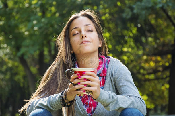 美丽的年轻女人在早晨的公园里喝咖啡