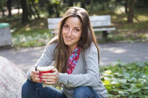 美丽的年轻<strong>女</strong>人在早晨的公园里喝咖啡