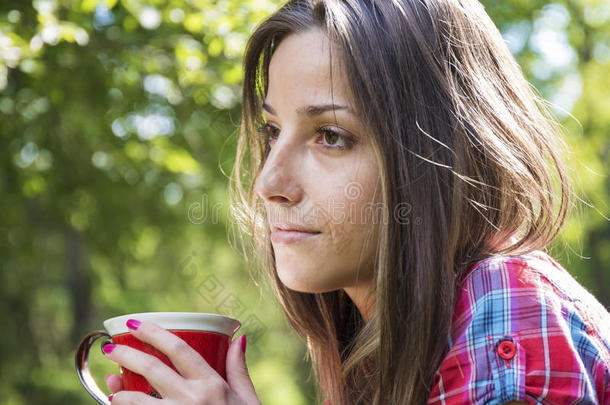 美丽的年轻女人在早晨的公园里喝咖啡