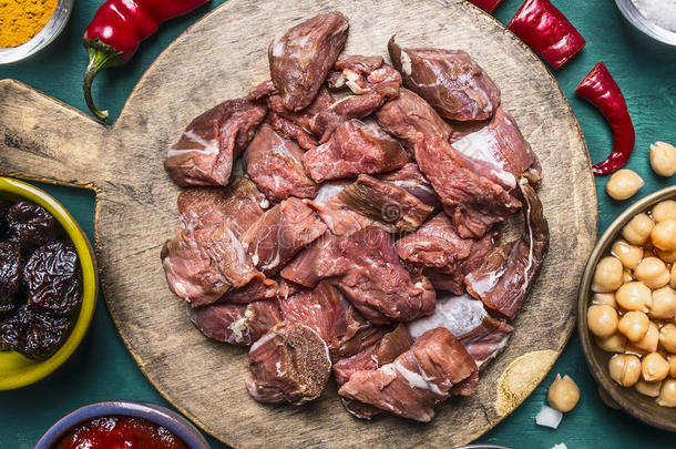 新鲜生羊肉与西梅部分红椒洋葱番茄酱罐头鹰嘴豆在一个切割板上的木制乡村背景