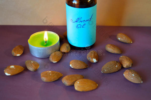一瓶杏仁油，散落的杏仁和紫色表面的小蜡烛