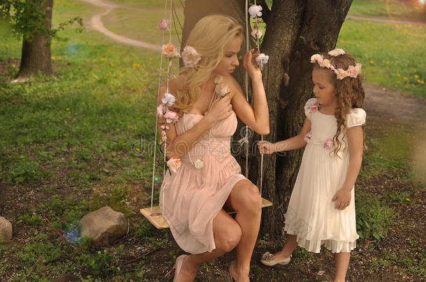 一个美丽的金发母亲，一个小女儿女孩依偎在绿色和紫色的花朵和五颜六色的肥皂b的自然背景上
