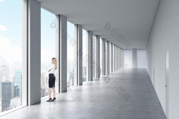 一个穿着正式衣服的女人正朝窗外看。 空的现代明亮清洁的内部开放空间办公室。 巨大的<strong>全景</strong>