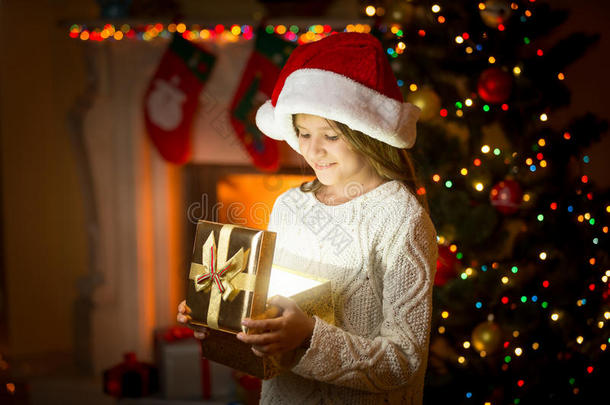 戴着圣诞老人帽子的女孩拿着发光的礼物盒