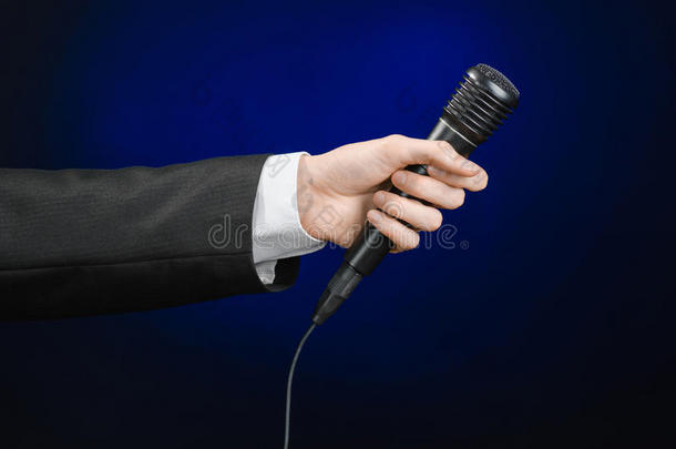 商务演讲和<strong>话题</strong>：一个穿着黑色西装的人，拿着一个黑色的麦克风，背景是深蓝色的，在演播室里孤立无援