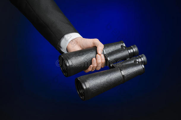 商业和搜索主题：穿着黑色西装的男人手里拿着一架黑色双筒望远镜，背景是深蓝色的，在工作室里被隔离