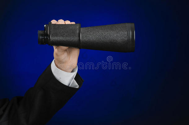 商业和搜索主题：穿着黑色西装的男人手里拿着一架黑色双筒望远镜，背景是深蓝色的，在工作室里被隔离