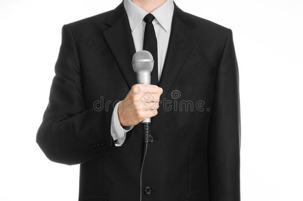 商业和演讲主题：穿黑色西装的人在演播室的一个孤立的白色背景上拿着一个灰色的麦克风