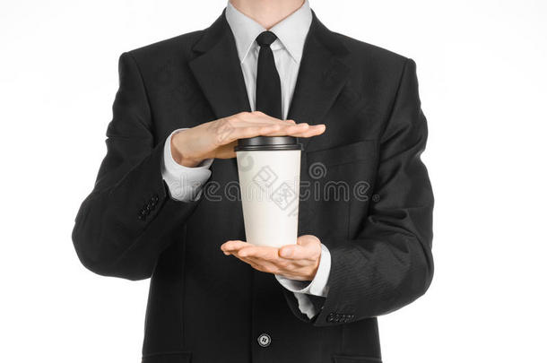商务午餐咖啡主题：穿黑色西装的商人拿着一杯白色空白纸杯咖啡和一顶棕色塑料帽