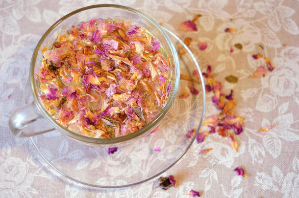 柔和的茶玫瑰花瓣饮料，透明的杯子和茶托和散落的花瓣复古颜色