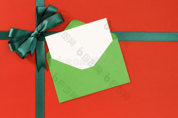 圣诞卡，红色礼品包装纸背景，绿色礼品丝带蝴蝶结，信封，复印空间