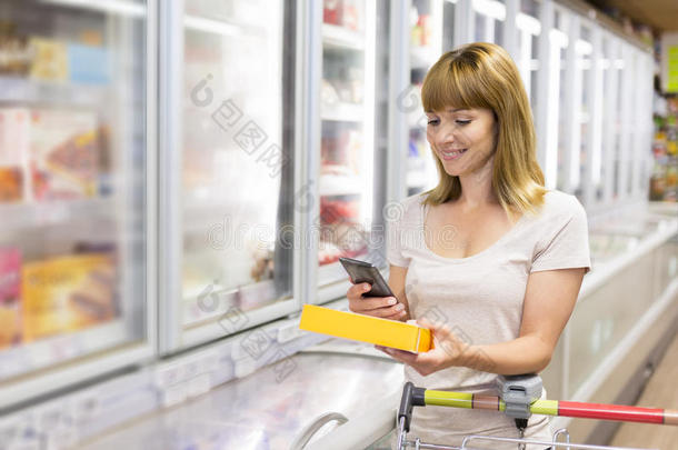 快乐的年轻女人在超市用手机发短信。