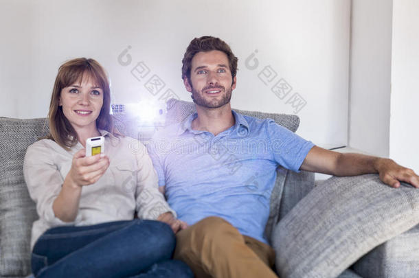 一对夫妇用视频投影仪在舒适的沙发上看电影