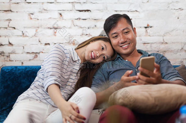 亚洲夫妇坐在沙发上使用手机智能手机