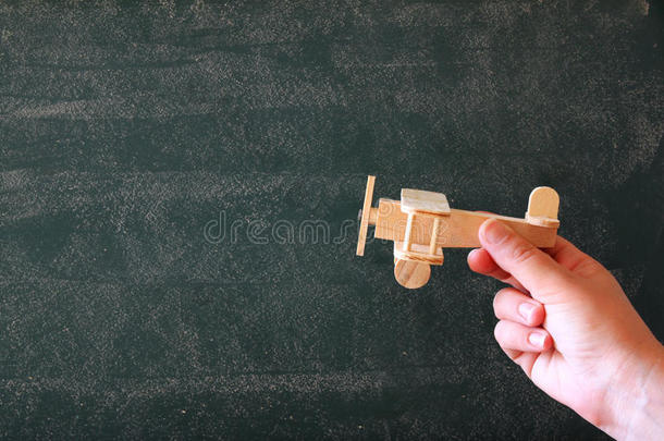 特写照片，女人的手拿着木制玩具飞机在黑板上。 灵感概念