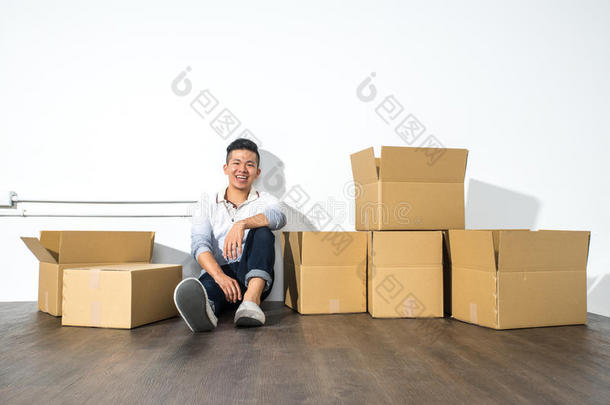 一个年轻的亚洲男人坐在地板上，笑着拿着盒子