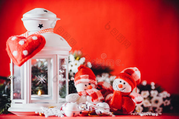 可爱的一对小雪人站在白色仙女灯笼附近，上面有一颗玩具心，装饰着杉木树枝。