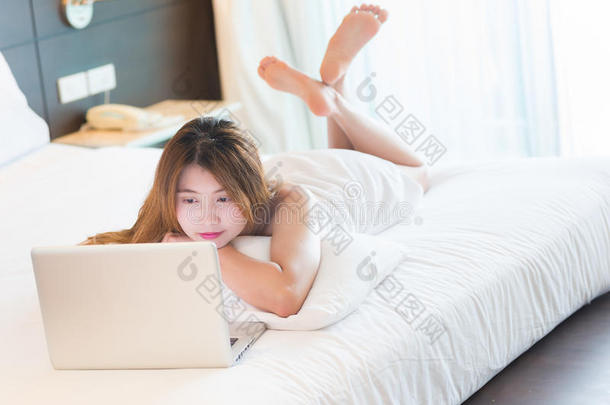 穿着浴袍的漂亮年轻女人在床上用笔记本电脑工作