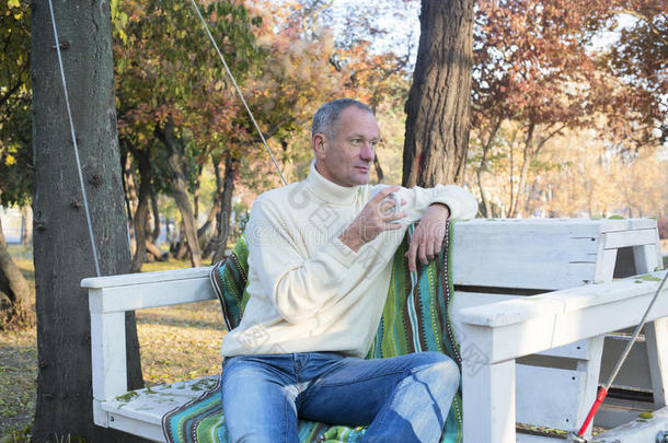 一个人在秋天的<strong>公园里</strong>用咖啡放松，<strong>坐在</strong>S上