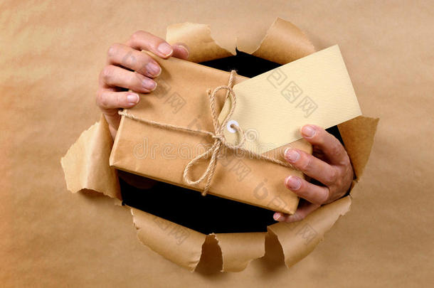 快递员或邮递员通过撕破的棕色纸背景递送或送包裹