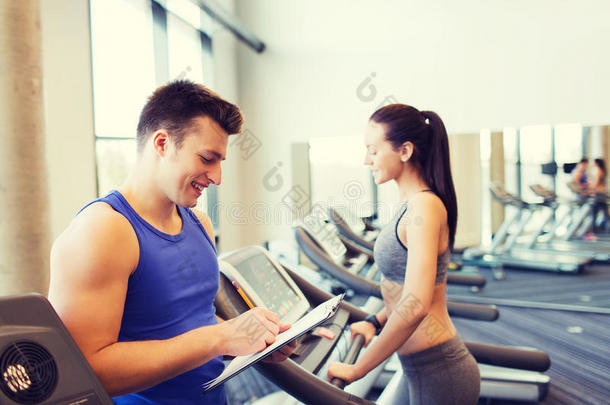 快乐的女人和教练在健身房跑步机上