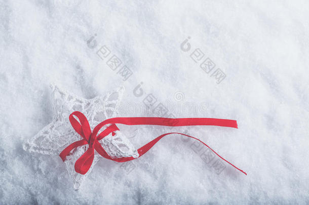 美丽神奇的老式白色星星，在白色的雪背景上系着一条红色的丝带。 冬天和圣诞节的概念。