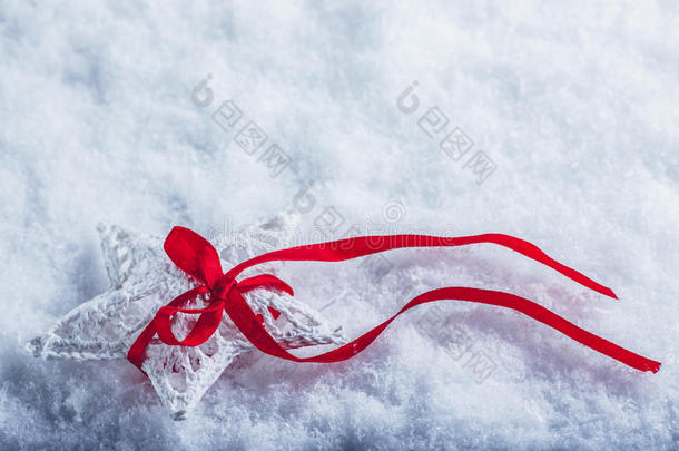 美丽神奇的老式白色星星，在白色的雪背景上系着一条红色的丝带。 冬天和圣诞节的概念。