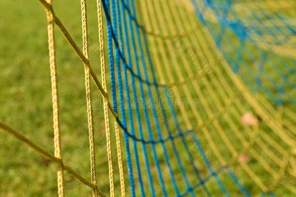黄色蓝色交叉<strong>足球</strong>网的细节，<strong>足球</strong>在<strong>球门</strong>网与可怜的草地在操场的背景。