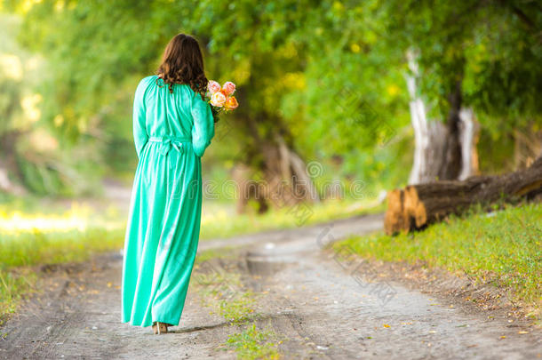 一个穿着长裙带着一束花的女孩在通往远方的路上