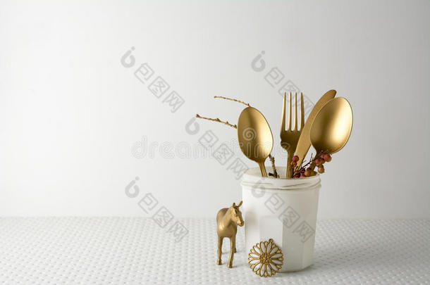 节日黄金餐具刀叉勺子在一个白色的瓶子，轻背景