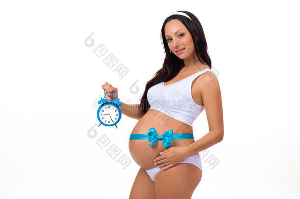 9个月。 快乐的怀孕。 孕妇手里拿着闹钟，肚子上有蓝色的蝴蝶结