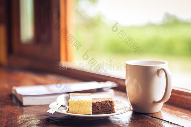 蛋糕和咖啡杯放在靠近窗台的木桌上。时间wi