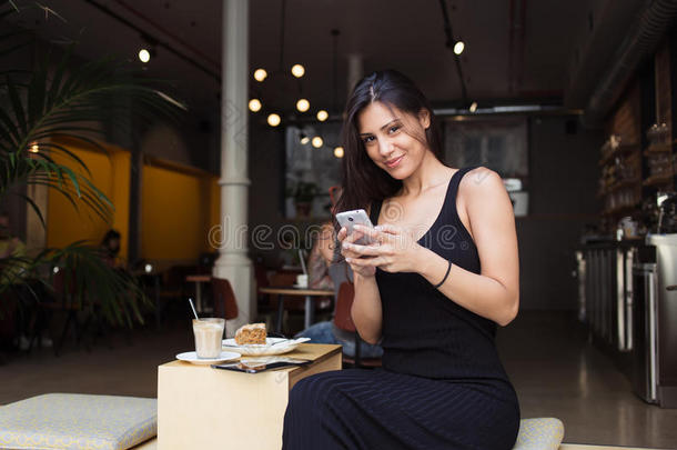 漂亮的女学生在讲课后在人行道咖啡馆放松的时候，拿着电话看着你