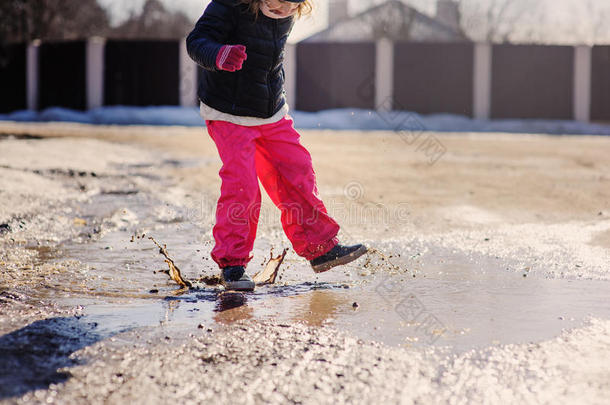 穿着防水裤子的女孩在冬天的散步中跳进水坑