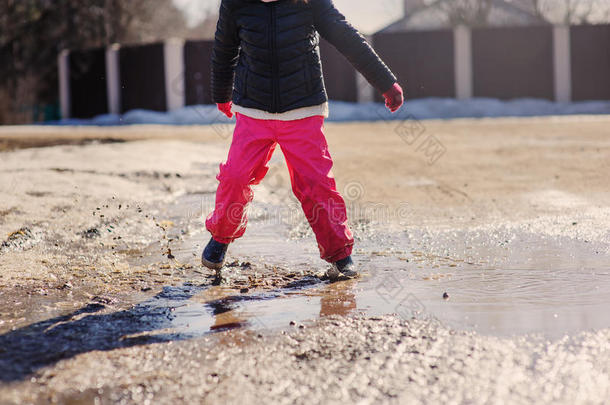 穿着防水裤子的女孩在冬天的散步中跳进水坑