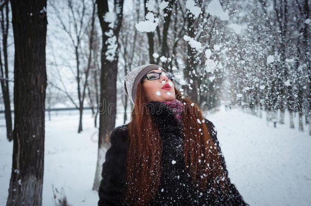 美丽的冬天女孩在寒冷的冬天公园里吹雪