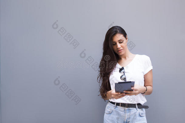 迷人的拉丁女人拿着她的数字平板电脑，站在街道墙壁背景下，为你提供复制空间