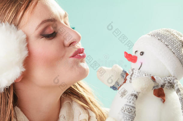 可爱的女人亲吻小雪人。 冬天的时尚。