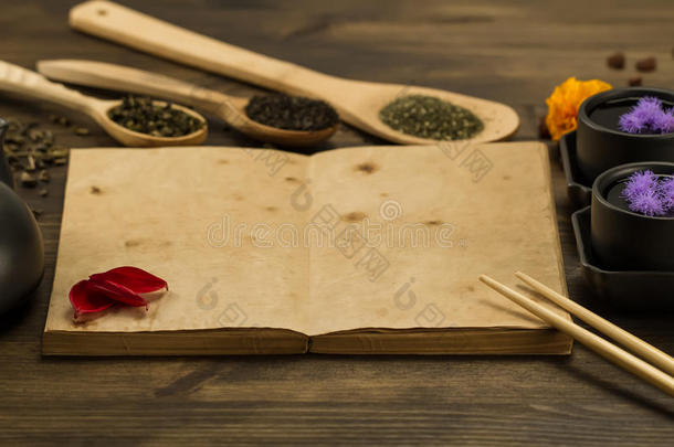 黑色茶壶，两个杯子，采茶，花，木制背景上的旧空白打开书。