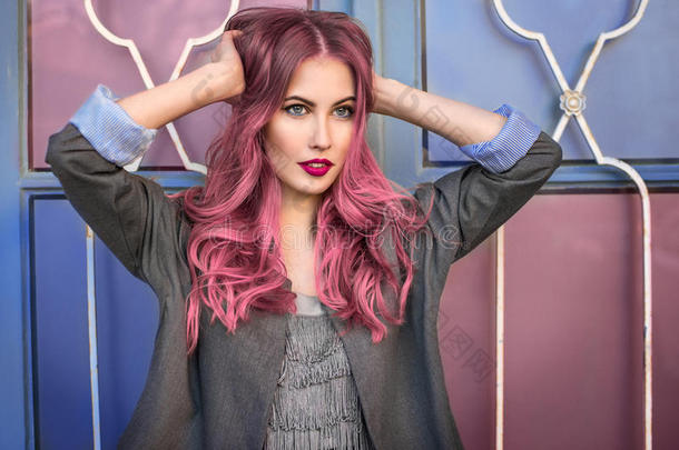 美丽的时尚模特，卷曲的粉红色头发摆在五颜六色的墙上