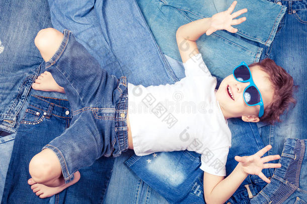 背景牛仔裤上戴着太阳镜的可爱小男孩。