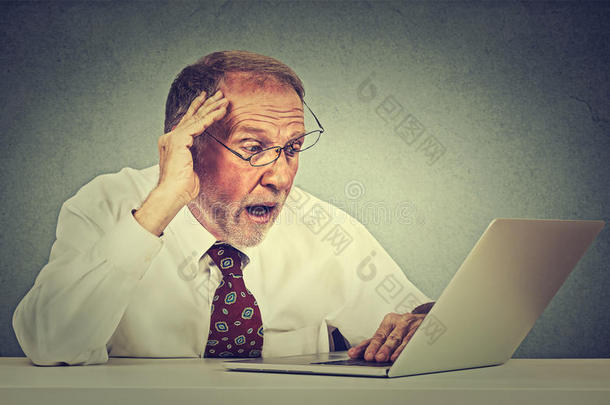 焦虑的老人看着笔记本电脑屏幕，看到坏消息，脸上带着令人厌恶的情绪