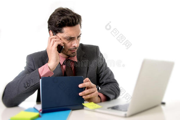 有吸引力的商人坐在办公桌前工作，压力很大，在电脑上，笔记本电脑上，在手机上