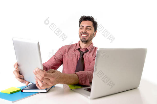商人在办公桌上工作，使用数字平板电脑垫微笑，快乐地坐在电脑笔记本电脑前，看上去很满意