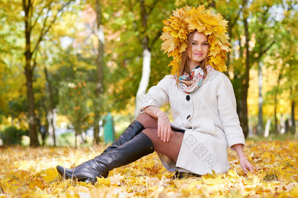 女孩坐在阳光明媚的秋天城市公园的树叶上