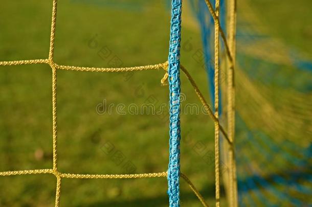 黄色蓝色交叉足球网的细节，足球在球门网与可怜的草地在操场的背景。