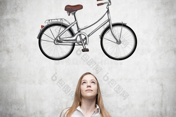 一个穿着正式衣服的女孩正在梦想一辆新自行车。 自行车的草图画在混凝土墙上。