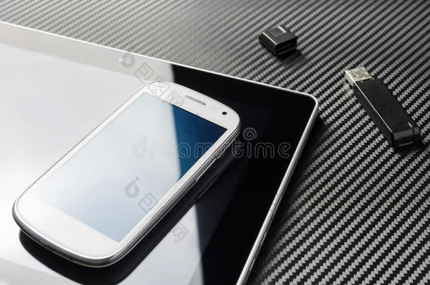 空白智能手机与蓝色反射躺在商务平板电脑旁边的一个开放的USB存储闪存驱动器以上的碳背景