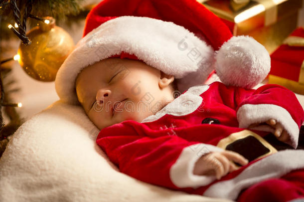 穿着圣诞老人服装的小男孩躺在圣诞树下。 圣诞节